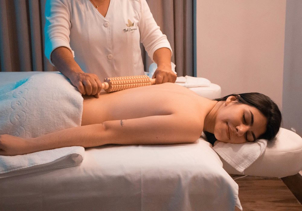 Therapist working along a guest’s back with a wooden roller during a full body session