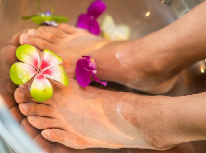 Pair of feet resting in a bowl of water scattered with orchid petals